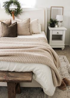 a bed with pillows and blankets on top of it next to a wooden bench in front of a window