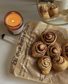 some cinnamon rolls sitting on top of a piece of newspaper next to a candle and mirror