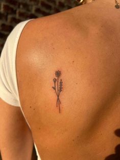 the back of a woman's shoulder with a small flower tattoo on her left side