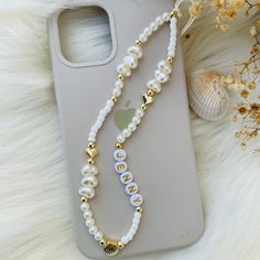 a cell phone case with a white beaded necklace and shell charm on it, next to some seashells