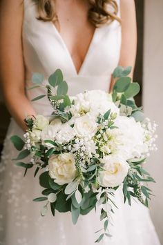 a bride holding a bouquet of white flowers and greenery