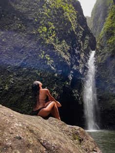 a woman sitting on top of a rock next to a waterfall