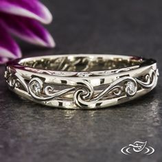 a close up of a wedding ring on a table with purple flowers in the background