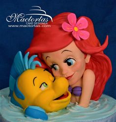 the little mermaid and the fish are hugging each other on top of a blue cake