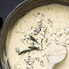 a pot filled with cheese and herbs on top of a stove next to a wooden spoon