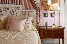 a bedroom with pink walls and floral bedding in front of a gold framed mirror