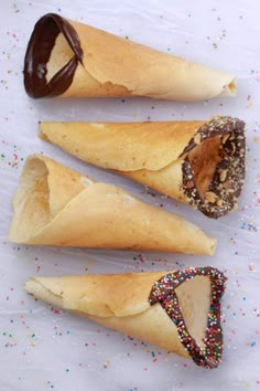 three pastries with chocolate and sprinkles are on a white tablecloth