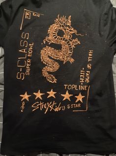 a black t - shirt with gold dragon and stars on the front is laying on a bed