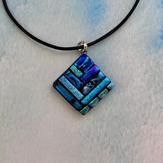 a blue and green square pendant on a black cord