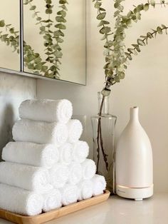 white towels are stacked on a tray next to a vase with flowers and a mirror in the background