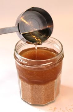 a spoon is pouring peanut butter into a jar with some brown stuff in it on a white surface