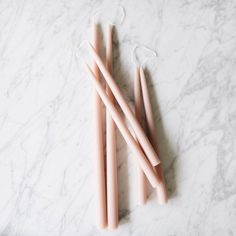 three pink candles sitting on top of a white counter next to a pair of scissors