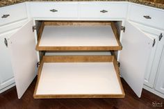 an open cabinet door in the corner of a kitchen with wood floors and white cabinets