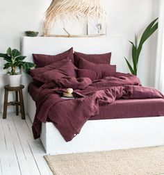 a bed with red sheets and pillows in a room next to a potted plant