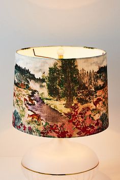 a lampshade with a painting on it sitting on a table next to a lamp