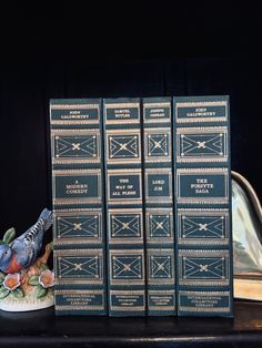 three blue books sitting on top of a table next to a silver vase with flowers