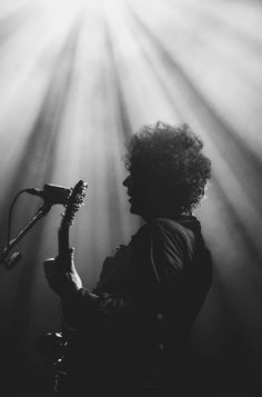 a black and white photo of a person playing a guitar in front of a microphone