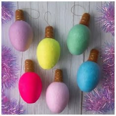 four different colored ornaments hanging from purple tinsel