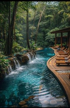 an outdoor swimming pool surrounded by lush green trees and water features wooden lounge chairs on either side