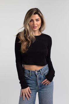 a woman wearing jeans and a black crop top with her hands on her hips, looking at the camera