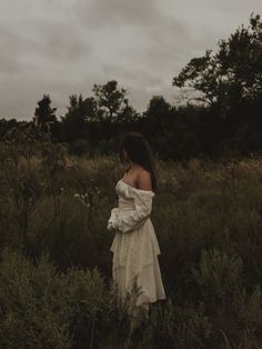 a woman in a white dress is standing in tall grass and looking off into the distance