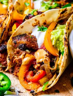 three tacos with meat, peppers and guacamole on a cutting board