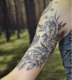 a woman's arm with flowers and leaves on it, in front of trees