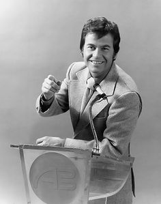 a man in a suit and tie standing at a podium with his hand on the microphone