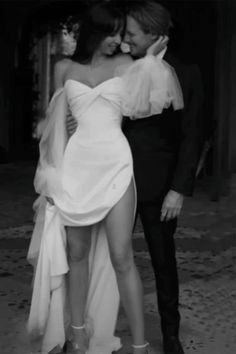 a man in a tuxedo hugging a woman in a white dress and high heels