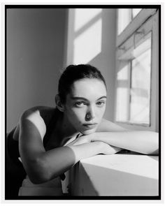 a black and white photo of a woman leaning on a window sill