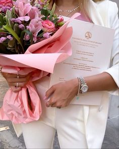 a woman holding a bouquet of flowers in her right hand and wearing a white suit