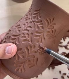 a person is working on a clay vase with a paintbrush in their left hand