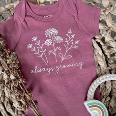 a baby bodysuit that says, always growing on it next to some dried flowers