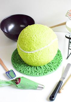 a tennis ball cake sitting on top of a green plate next to utensils