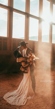 a bride and groom standing in front of large windows with sun coming through the window