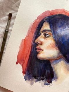 a watercolor painting of a woman's face on paper next to a brush