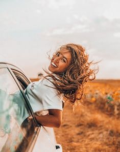 a woman leaning out the window of a car with her hair blowing in the wind