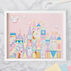 a pink and yellow paper cutout of a castle on a marble surface with pastel colors