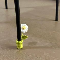 a small crocheted flower in a yellow vase on the floor with black poles