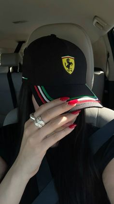 a woman wearing a ferrari hat covering her face in the back seat of a car