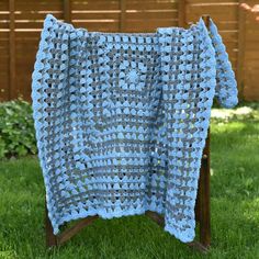 a blue crocheted afghan sitting on top of a wooden chair in the grass