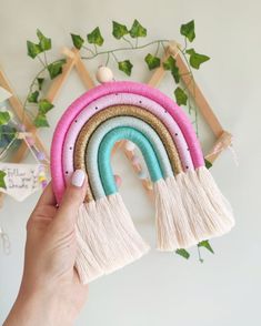 a person holding up a rainbow decoration with tassels