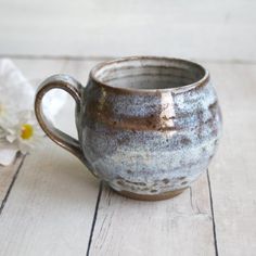 a brown and white cup sitting on top of a wooden table next to a flower