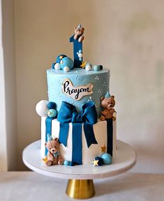 a blue and white baby shower cake with teddy bears on the top, sitting on a gold pedestal