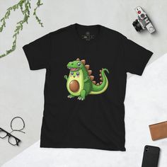 Step into the whimsical world of healthy fun with our exclusive 'Avocadosaurus' T-shirt - where a friendly cartoon-style avocado dons a dinosaur costume, adding a playful twist to your wardrobe! 🥑🦕 This delightful design isn't just about clothing; it's a wearable celebration of health and happiness, bringing a smile to your face with every wear. It's more than an article of clothing; it's a fashion statement, a nod to the joy of good nutrition, and an invitation to embrace the lighthearted spirit within. 🥑✨ Immerse yourself in the charm of our design, where the 'Avocadosaurus' steals the spotlight, dressed in a dinosaur costume that adds a burst of color and fun. The print captures every adorable detail, from the avocado's happy expression to the quirky dinosaur spikes, ensuring this T- Fun Short Sleeve T-shirt With Dinosaur Print, Playful Dinosaur Print Crew Neck T-shirt, Green Funny Cartoon Print T-shirt, Funny Green Cartoon Print T-shirt, Playful Cotton T-shirt With Dinosaur Print, Novelty Cartoon Print Short Sleeve T-shirt, Novelty Short Sleeve T-shirt With Cartoon Print, Funny Black T-shirt With Dinosaur Print, Funny Dinosaur Print Short Sleeve T-shirt