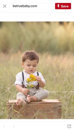 a little boy sitting on top of a wooden crate holding a flower in his hands