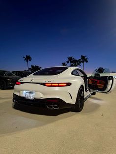 the rear end of a white sports car parked in a parking lot next to palm trees