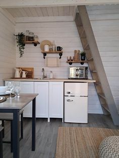 a small kitchen with white cabinets and wooden stairs leading up to the loft above it