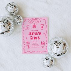 a pink birthday party card with disco balls and confetti on the table next to it