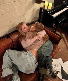 two women hugging each other while sitting on a leather couch in front of a piano